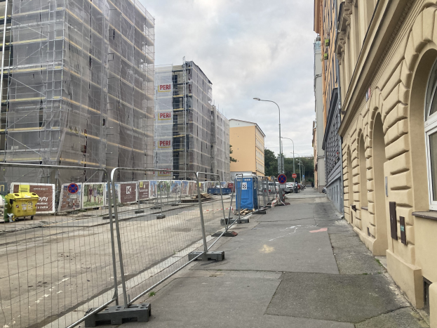 City street with buildings, vehicles, street infrastructure, trees, and a construction site with scaffolding.