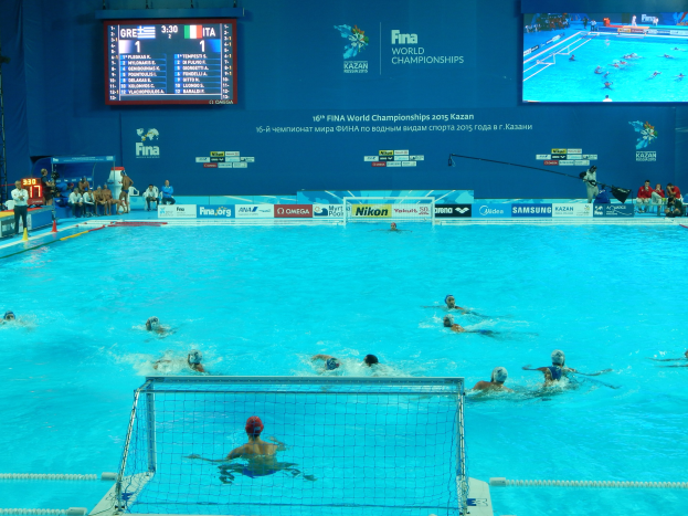 Eine Gruppe von Menschen spielt Wasserball in einem Pool während der FINA-Weltmeisterschaften 2016 in Kazan, mit einem Netz, das den Pool teilt, und Zuschauern auf der linken Seite.