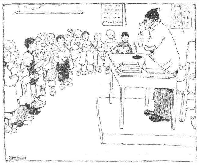 Mann in Schuhen sitzt an einem Schreibtisch mit Büchern und Gegenständen, gegenüber einer Gruppe von Kindern, mit Papieren an der Wand dahinter.