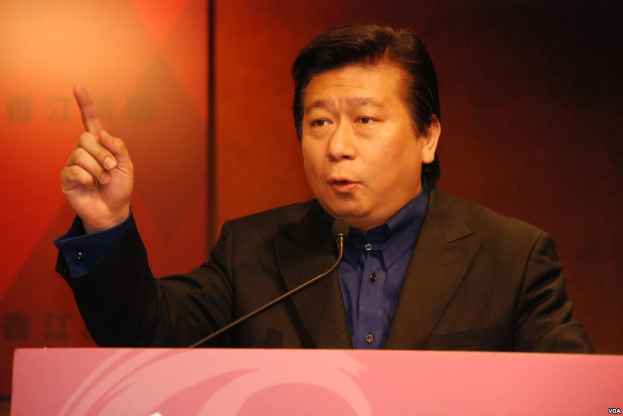 A man in a suit and tie giving a speech at a podium with a microphone, appearing serious.