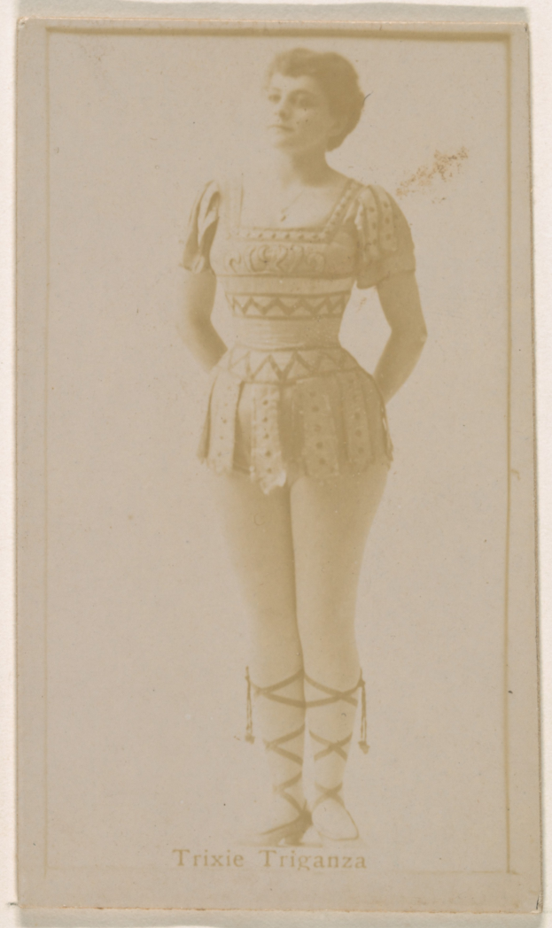 Ein altes Foto einer Frau in einem hellfarbenen gemusterten Badeanzug, ihre Haare zu einem Dutt gebunden, die mit einem leichten Lächeln und direktem Blick in die Kamera steht.