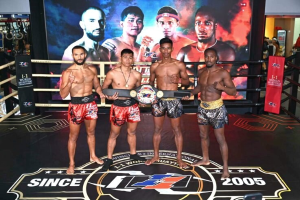 Four men in a boxing ring hold championship belts while a "Muay Thai World Championship" screen displays in the background.
