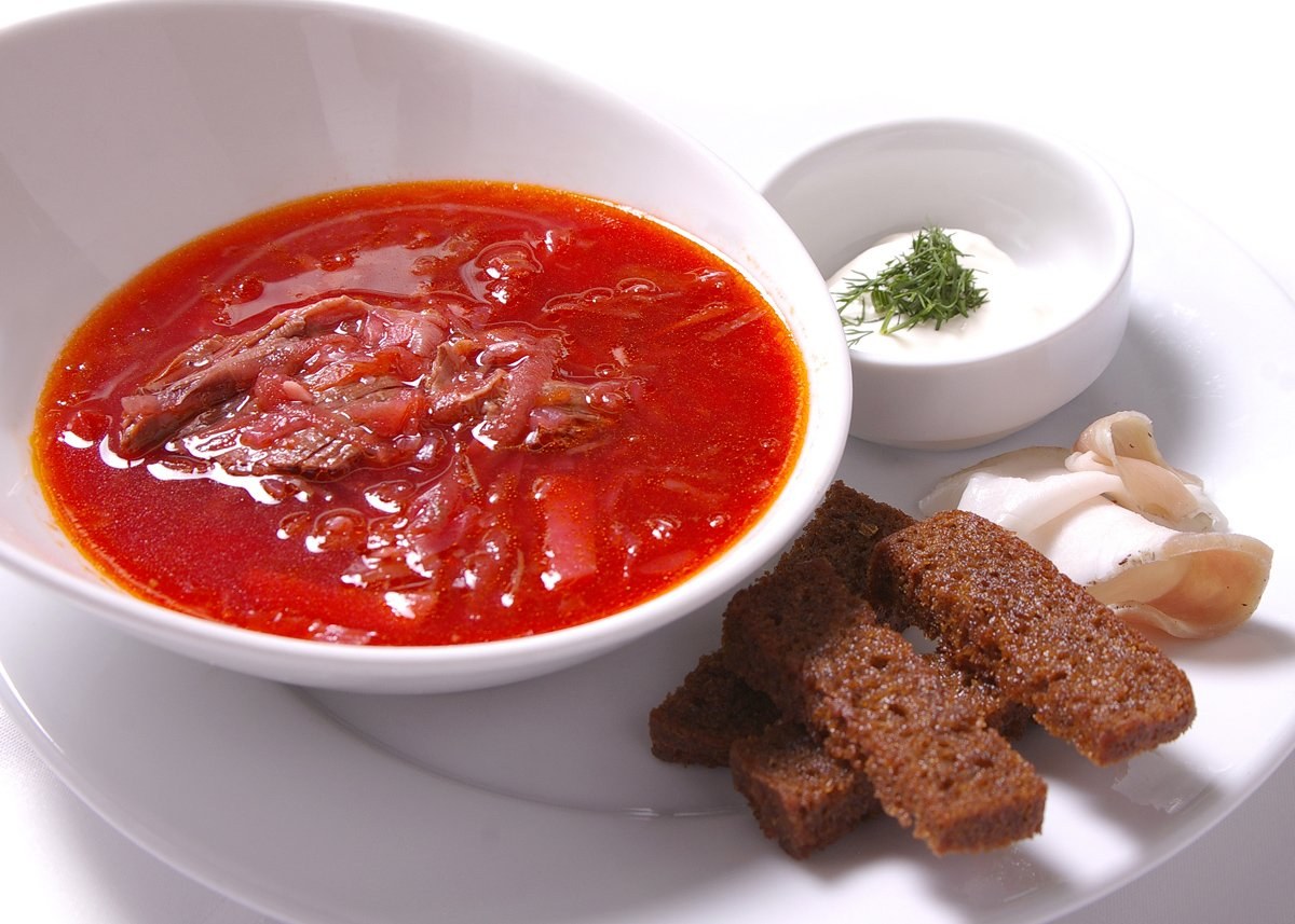 Ein weißer Teller mit einer Schüssel dicker roter Gazpacho-Suppe, leicht getoastetes Brot und Petersiliengarnitur.