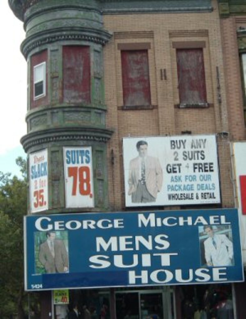 Ein Gebäude mit Plakaten an seiner Fassade, Stände unten, umgeben von Bäumen und Himmel.