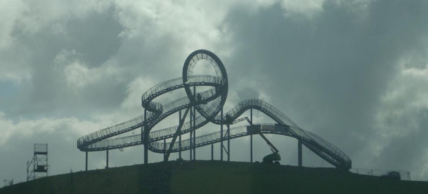 Eine Achterbahn auf dem Höhepunkt eines Hügels bei einem bewölkten Himmel mit sichtbaren Stützpfählen und -strukturen.