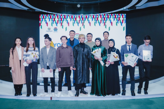 Gruppe von Menschen auf einer Bühne mit Blumensträußen und Urkunden, im Hintergrund ein 'Jugend-Solar-Awards 2019'-Plakat.