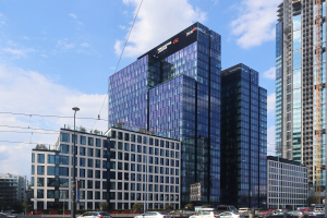 Zentrale der Deutschen Bank in Frankfurt, Deutschland, ein großes mehrstöckiges Gebäude mit zahlreichen Fenstern, umgeben von städtischer Infrastruktur einschließlich Straßenlaternen, elektrischen Kabeln, Fahrzeugen, Grünflächen und einem bewölkten Himmel.