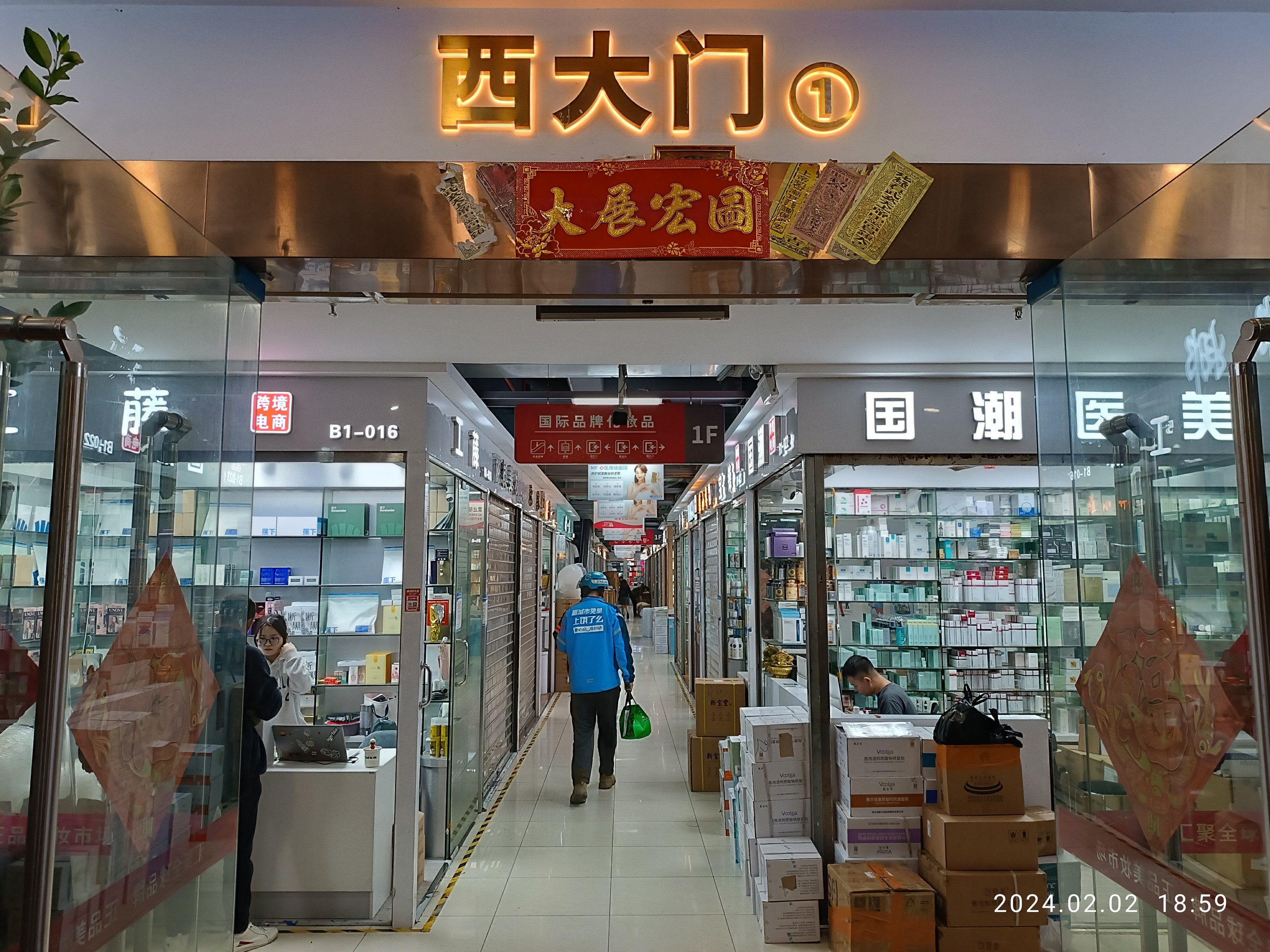 Interior of a Chinese pharmacy with glass walls, shelves stocked with items, scattered cardboard boxes, a plant on the left, and a name board at the top.