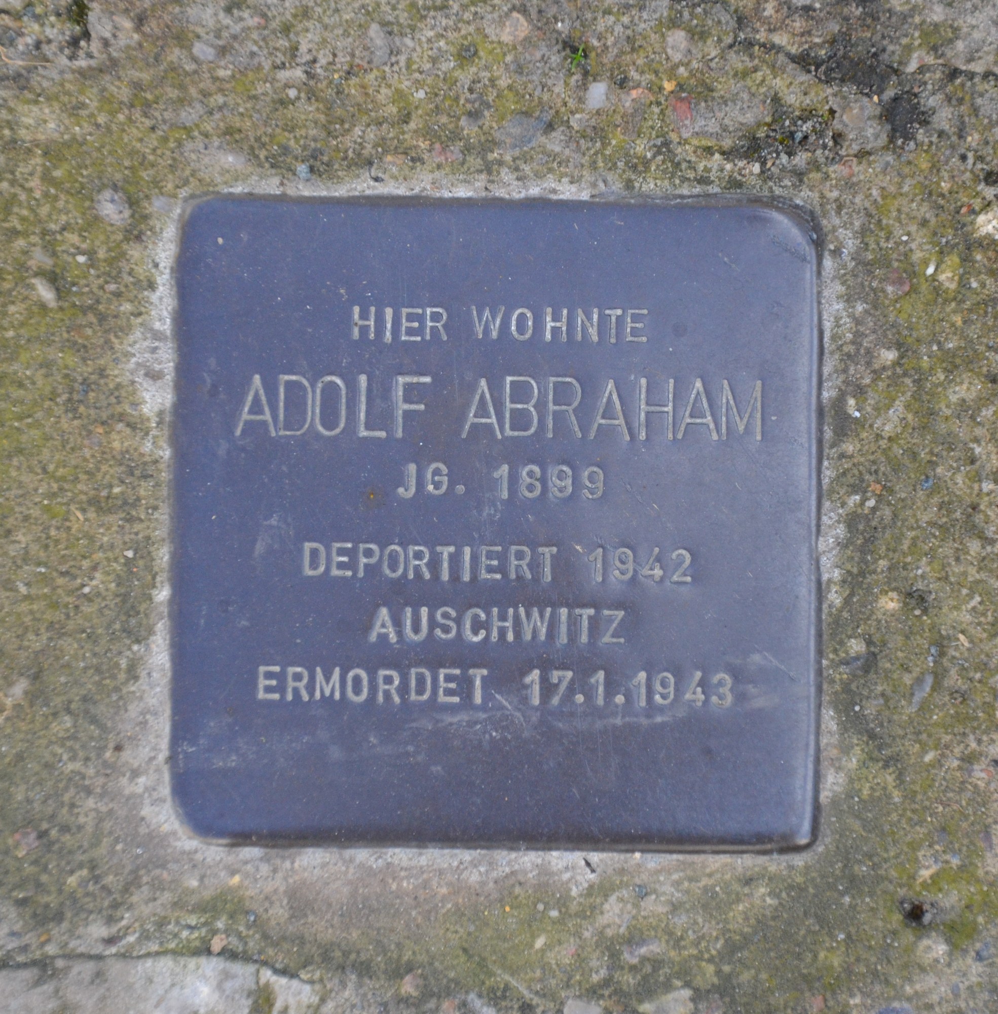 Rechteckige Plakette mit der Inschrift "Adolf Abraham" an einer Steinwand befestigt.