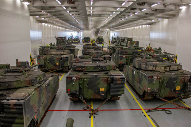 Ein grosser Militaraerraum mit Reihen von Militaraerfahrzeugen, beleuchtet von Deckenleuchten und begrenzt von Waenden.