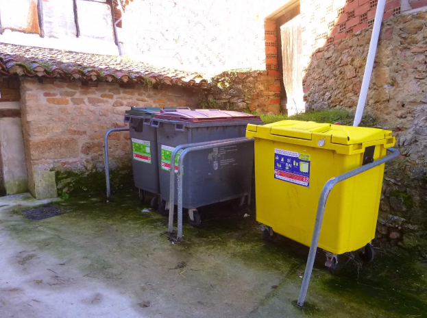 Zwei gelbe und graue Mülltonnen mit Rädern nebeneinander vor einem Gebäude mit Wand und Fenster positioniert.