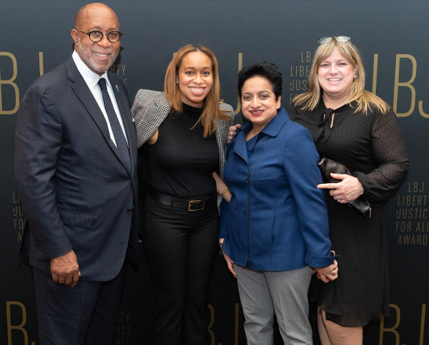 Vier Personen auf einem roten Teppich, die fröhlich posieren und für ein Foto posieren.