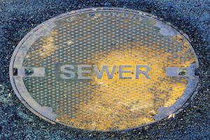 Metallschachtdeckel auf einer Straße mit der eingravierten Aufschrift "Abwasser"