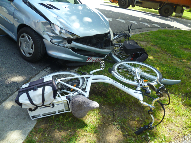 Auto am Straßenrand mit einem Fahrrad in der Nähe auf dem Gras, Bäume und ein klarer blauer Himmel im Hintergrund.