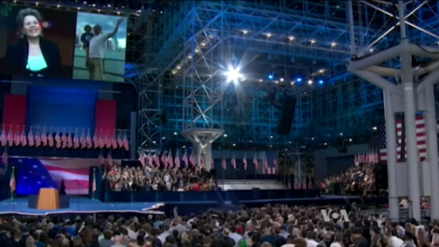 Eine große Menschenmenge vor einer Bühne mit einem Rednerpult, einem Mikrofon, Flaggen, einem Bildschirm und einer Lichtanlage, die auf eine Präsidentschaftsdiskussion warten.