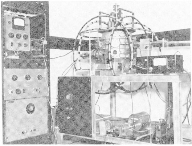 Black and white photo of an electron accelerator machine in a room with a wall in the background and text at the bottom.