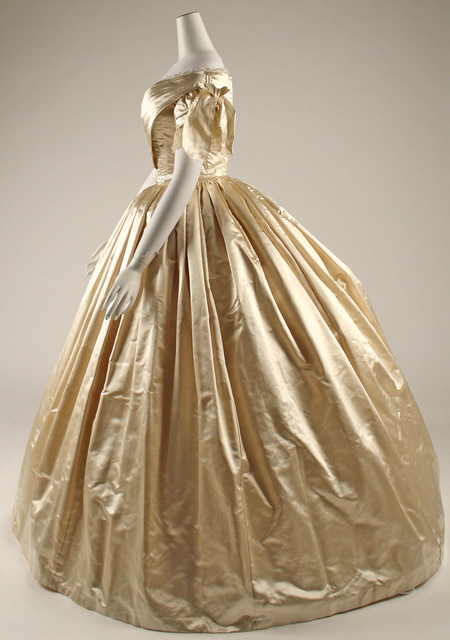 A gold ball gown with a high neckline, long sleeves, and a voluminous skirt displayed on a mannequin in a museum.