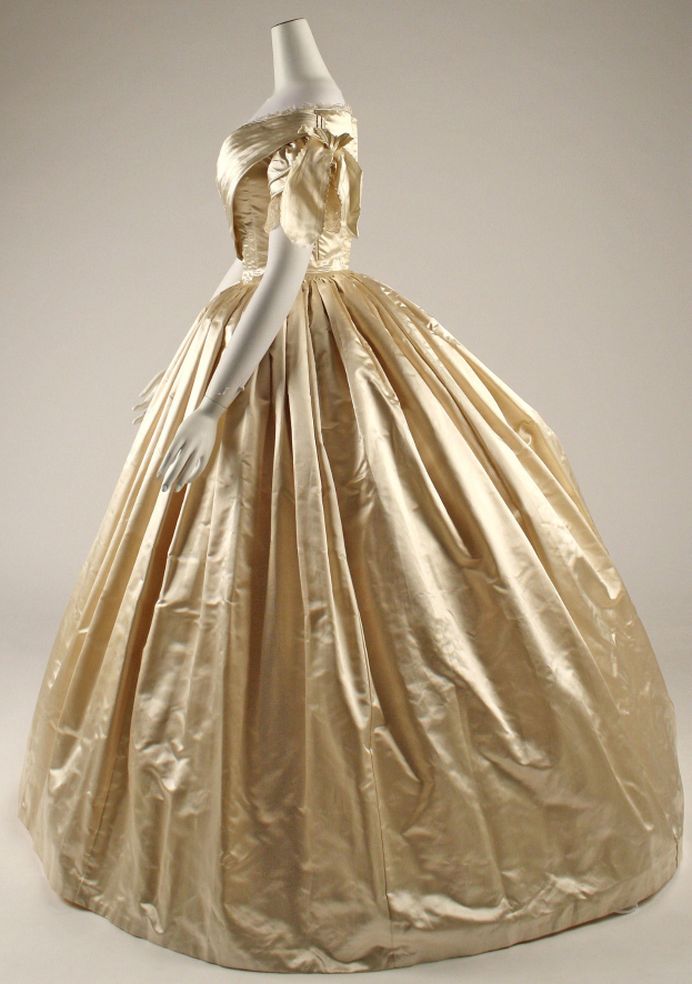 A gold ball gown with a high neckline, long sleeves, and a voluminous skirt displayed on a mannequin in a museum.