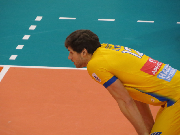 Eine professionelle Volleyballspielerin in einem gelben T-Shirt mit der Aufschrift "Volleyball" steht selbstbewusst auf einem Court und ist bereit zum Aufschlag.