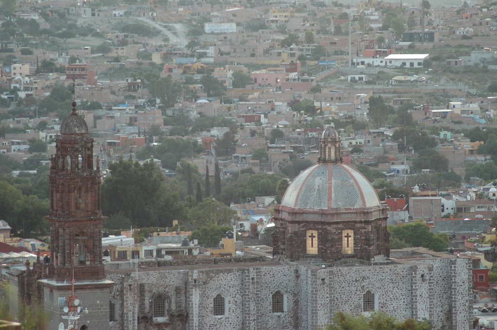 Luftbild einer Stadt mit einer Kirche im Vordergrund, das Bäume, Gebäude, Straßen und Masten zeigt.