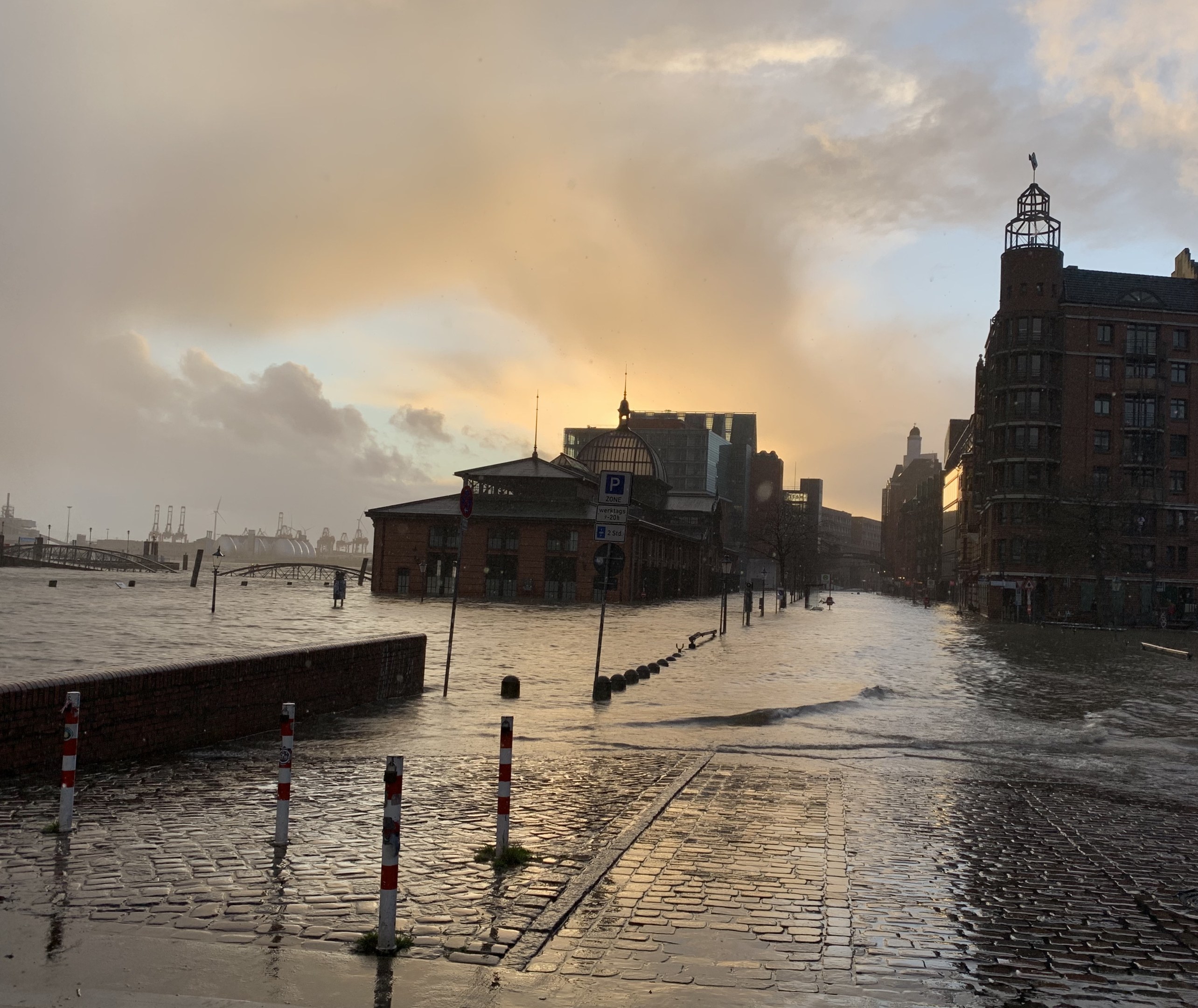 Überschwemmte Straße in Hamburg, Deutschland mit Wasser, das die Straße, Pfähle, Schilder, Gebäude und eine Brücke bedeckt.