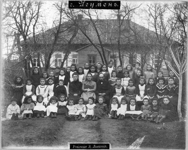 Schwarzes und weißes Foto von Kindern, die vor einem Fenster mit einem Gebäude posieren, umgeben von Bäumen und einem klaren Himmel, mit Text unten, der 'Jugoslawien, die erste Schule der Welt' liest.