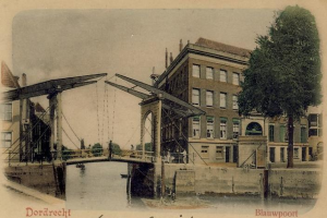 Altes Schwarz-Weiß-Foto einer Brücke, die einen Fluss überspannt, mit Gebäuden, Bäumen und einem klaren Himmel im Hintergrund und verstreuten Baumaschinen und Materialien am Flussufer.