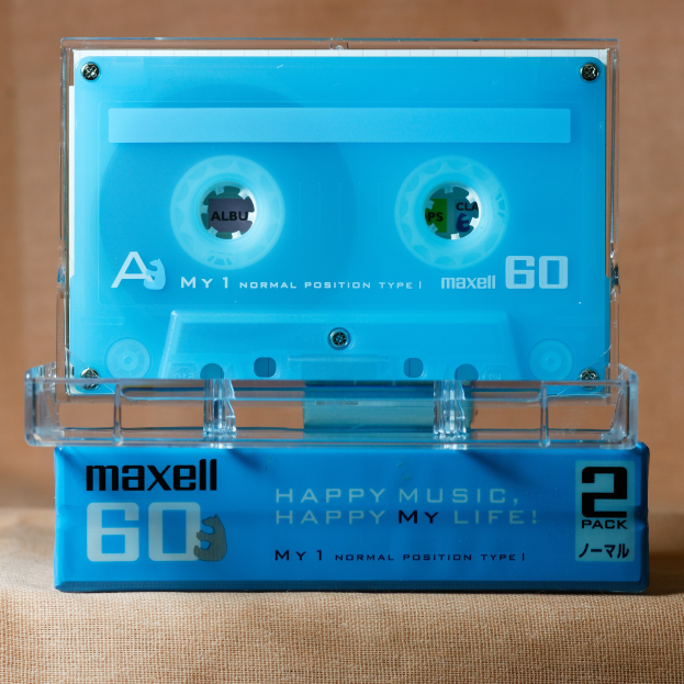 Eine blaue Maxell-Kassette mit der Aufschrift "Happy Music, Happy My Life" auf einer braunen Oberfläche.