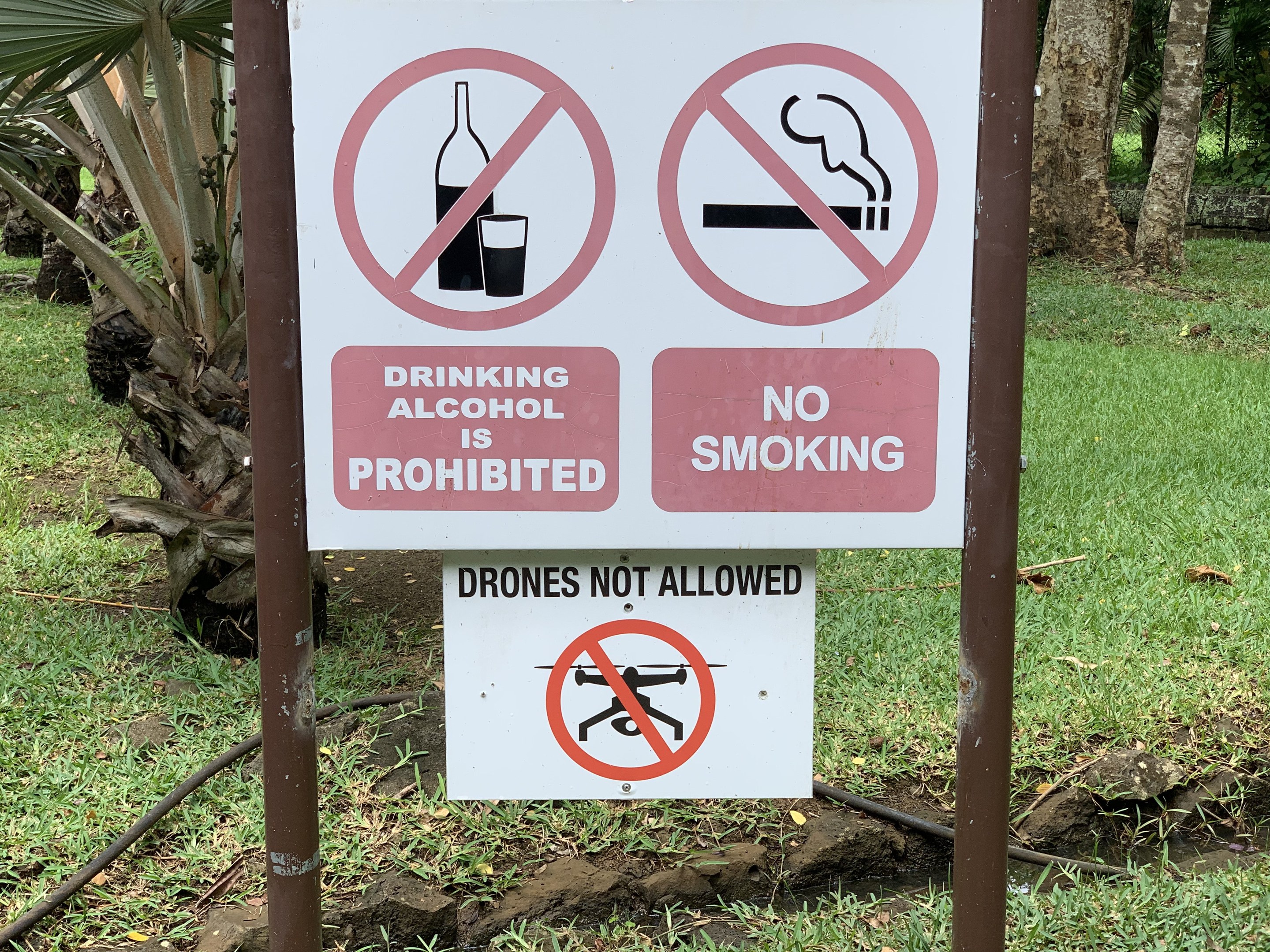 Sign on the roadside prohibiting drinking alcohol and smoking, with trees and grass in the background.