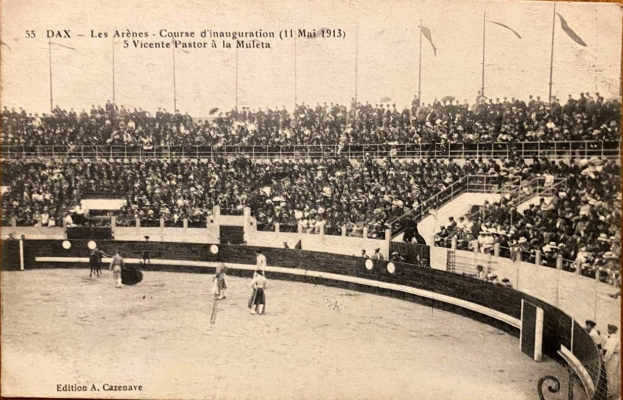 Schwarzes und weißes Foto eines Boxkampfes in einer Stadion mit Zuschauern auf den Tribünen und einer Gruppe von Menschen in der Mitte.