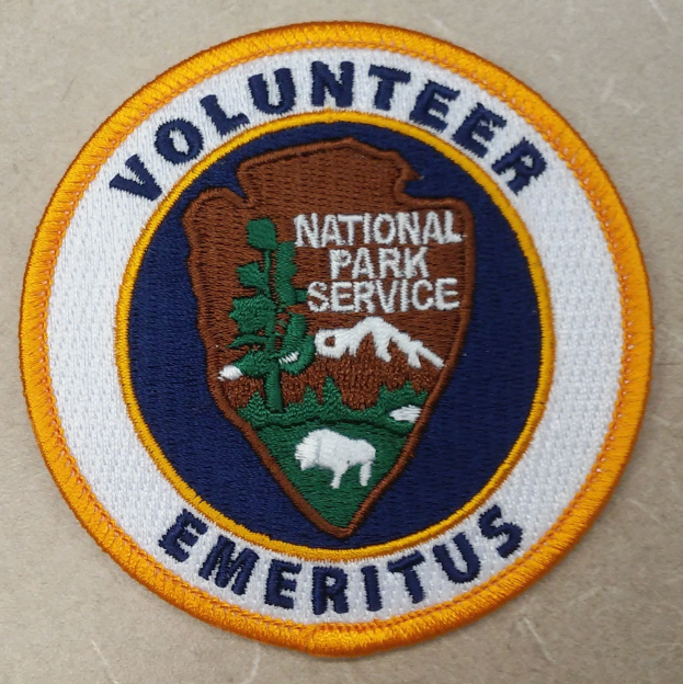 Runder Flicken mit einem blauen Rand und einem weißen Hintergrund, der den schwarzen Text "Volunteer National Park Service Emeritus" in der Mitte eines gelben Kreises zeigt.