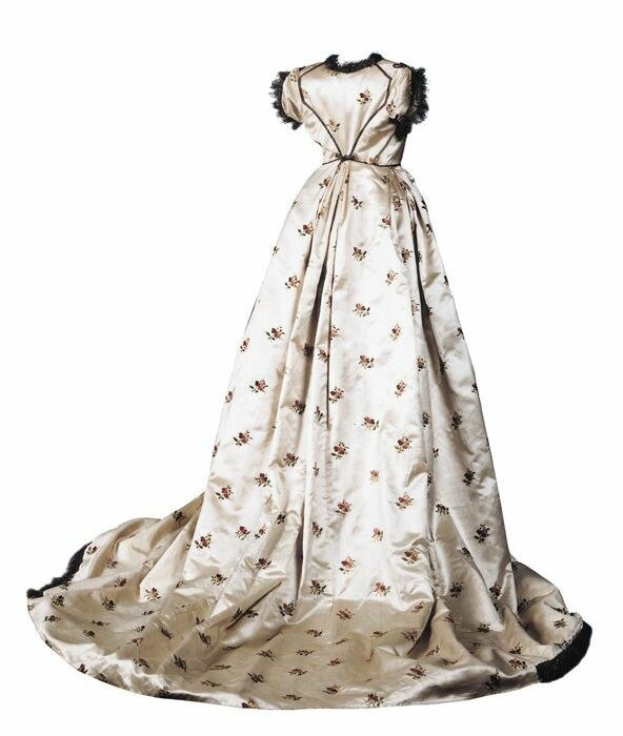 Weißes 18. Jahrhundert Hochzeitskleid mit schwarzem Saum, Herzausschnitt, eng anliegender Taille, voluminösem Rock und zarter floraler Stickerei auf leichtem, luftigem Stoff vor einem weißen Hintergrund.