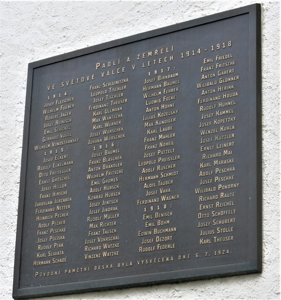 Dark plaque mounted on a building wall with bold text reading "Plaque for the victims of the Holocaust" surrounded by a decorative border.