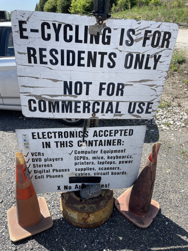 Schild mit der Aufschrift "E-Bike-Fahren nur für Anwohner" steht an einer Straße mit Verkehrskegeln in der Nähe, ein Fahrzeug im Hintergrund, Bäume und ein klarer blauer Himmel.