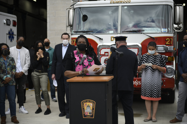 Bürgermeisterin Lori Lightfoot der Stadt Chicago spricht auf einer Pressekonferenz vor einem Feuerwehrauto, mit einer Gruppe von Menschen mit Masken, Mikrofonen auf Ständern, Papieren auf dem Podium und einer beleuchteten Wand im Hintergrund.