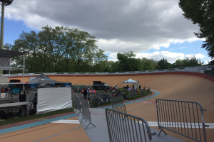 Gruppe von Radfahrern auf einer Schotterstrecke bei einem Outdoor-BMX-Event mit Zelten, Fahrzeugen und Bäumen im Hintergrund.