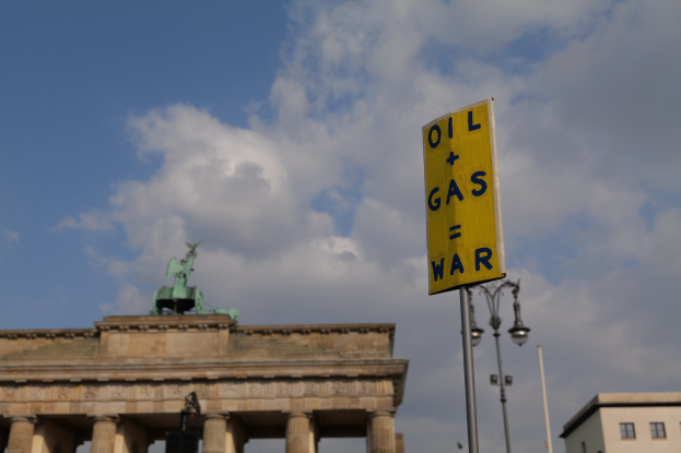 Das Brandenburger Tor in Berlin, Deutschland, mit einem gelben Schild, auf dem "Öl- und Gas-Krieg" steht, im Vordergrund, Gebäuden, Polen, Lampen, einer Statue und einem bewölkten Himmel im Hintergrund.