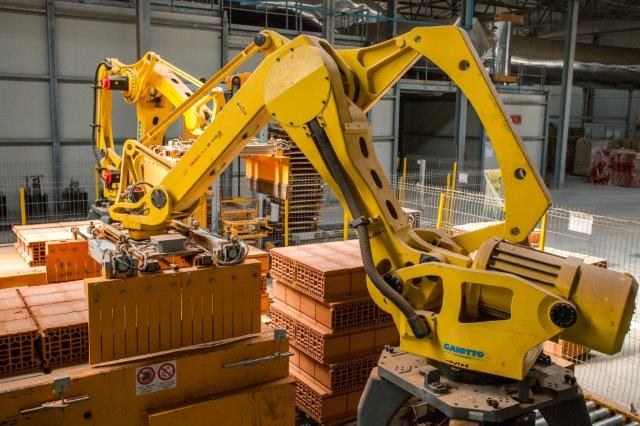 Industrielles Lagerhaus mit gestapelten Kisten, Kränen, Zaun, Pfählen und einer fernen Wand in einer Fertigungsanlage.