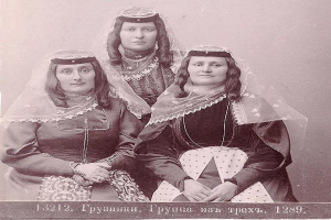 Drei Frauen in traditionellen russischen Hochzeitskleidern mit kunstvoller Stickerei und Perlen stehen vor einer weißen Wand, mit Text unten, der darauf hinweist, dass es ein russisches Hochzeitsfoto ist.