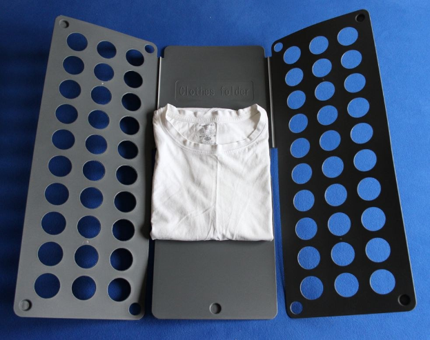 Weißes T-Shirt auf blauer Oberfläche neben einem schwarzen und grauen Kleiderordner mit mehreren Löchern.