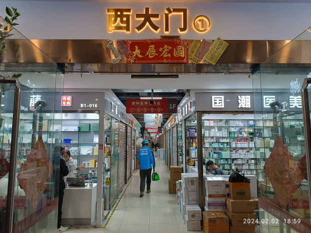Innenansicht einer chinesischen Apotheke mit Glaswänden, Regalen mit Artikeln, verstreuten Kartons, einer Pflanze auf der linken Seite und einem Namensschild oben.