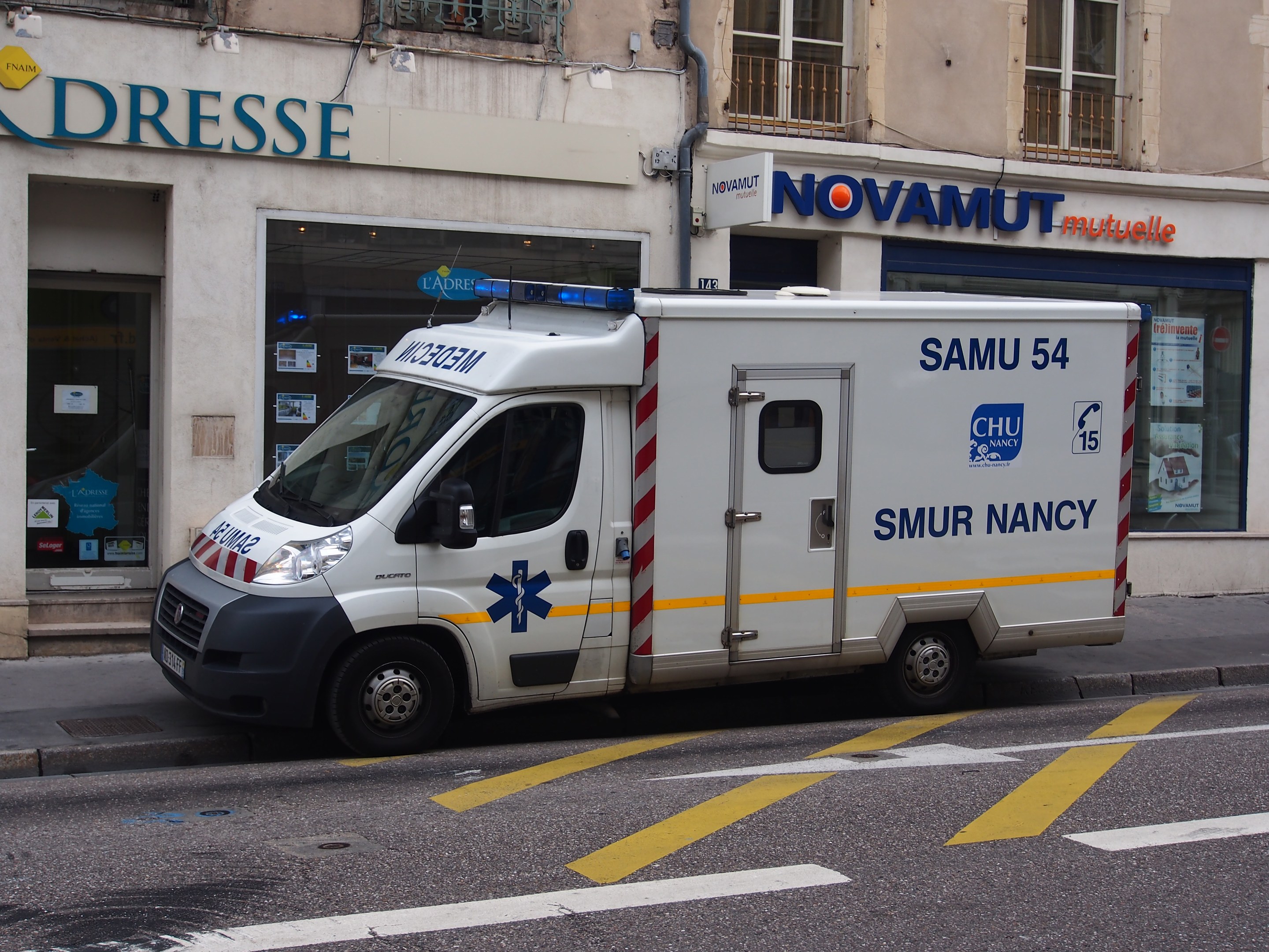 Ambulance parked in front of a hospital building with windows, railings, and posted signs.