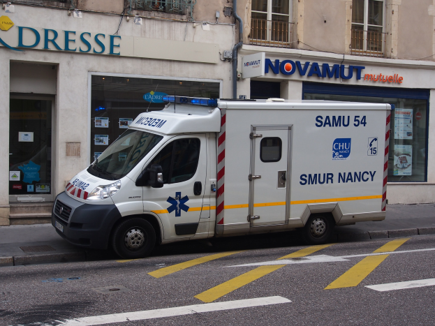 Ambulance parked in front of a hospital building with windows, railings, and posted signs.