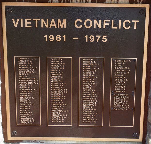 Plaque on a brick building commemorating the Vietnam Conflict from 1961 to 1975, with bold black text on a dark background and a decorative border.