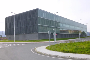 Ein großes, mehrstöckiges Gebäude mit zahlreichen Fenstern, das als neue Zentrale der Schwedischen Nationalen Universität für Wissenschaft und Technologie dient, umgeben von Straßeninfrastruktur, Grünflächen und einem klaren blauen Himmel.