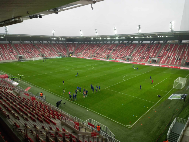 A soccer field in a stadium with spectators seated around it under stadium lights, with the sky visible in the background.