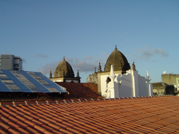 Stadtansicht mit mehreren Gebäuden im Vordergrund, einem blauen Himmel im Hintergrund und Solarpanels auf dem Dach eines Gebäudes.