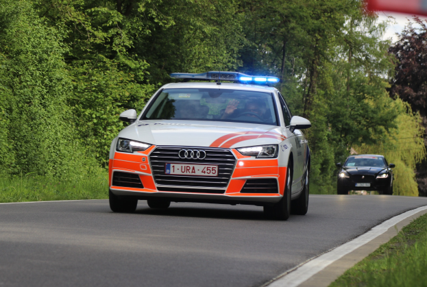 Ein Polizei-Audi A4 fährt auf einer grasbewachsenen Straße neben einem Wald mit zwei Personen darin, unter einem klaren blauen Himmel.