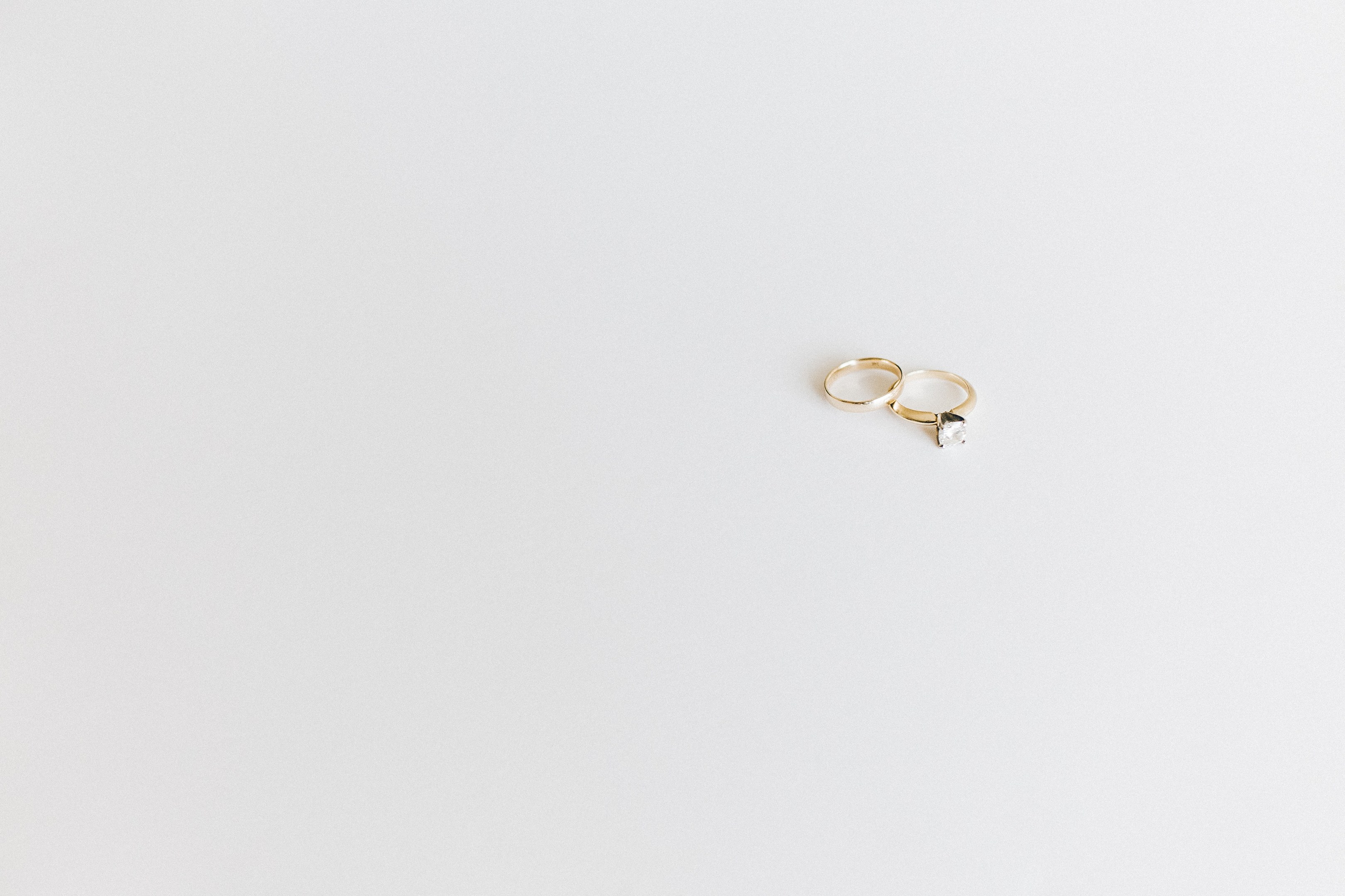 Two gold wedding rings with a single diamond each, set on a white surface, reflecting light.