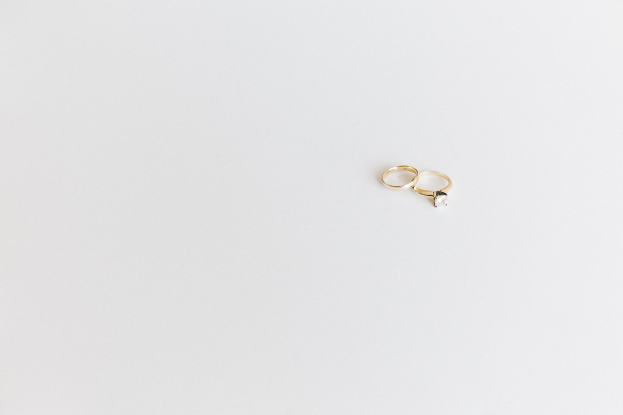 Two gold wedding rings with a single diamond each, set on a white surface, reflecting light.